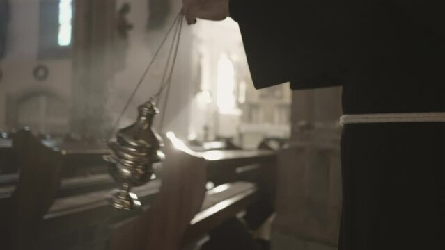 Christian monk holding thurible in hand and walking in church close up slow motion. Religious metal censer swinging in priest arm during worship ritual