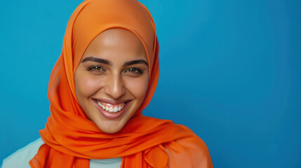 A positive Muslim woman smiles while wearing a traditional orange headscarf, looking directly at the camera