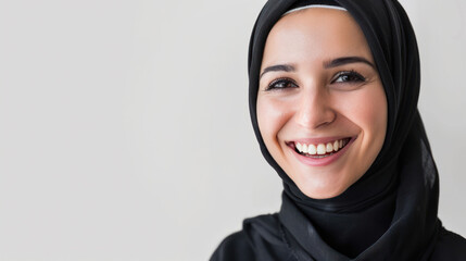 A positive Muslim woman happily smiling while wearing a traditional black hijab