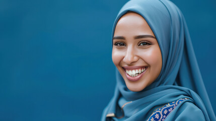 A positive Muslim woman is smiling while wearing a traditional blue headscarf