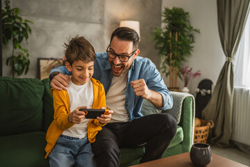 Father and son play video games on a mobile phone and enjoy at home