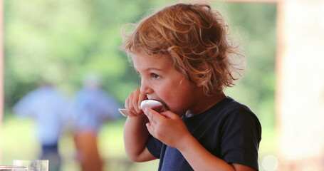 Little blond boy eating melon fruit dessert with spoon casual and candid