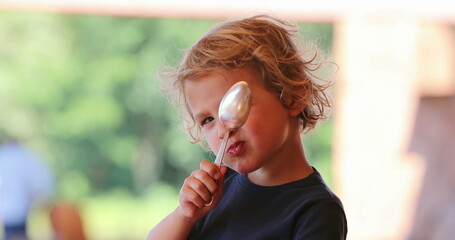 Little blond boy hiding from camera with hand and spoon being cute and adorable