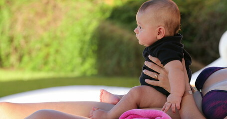 Mom holding baby son by the poolside outdoors