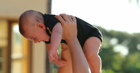 Mom lifting baby son upwards outdoors by the poolside