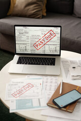 Unpaid financial bills, smartphone with calculator on screen, notepad lying next to laptop with...