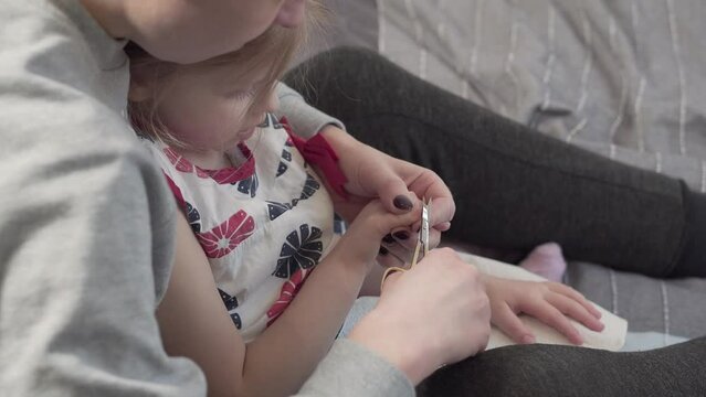 Mom cuts her little daughter's nails with scissors. Dirt under a little girl's nails.