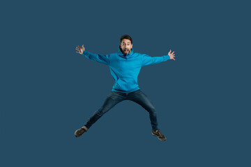 A man wearing a blue shirt is captured mid-air as he jumps energetically. His body is stretched...