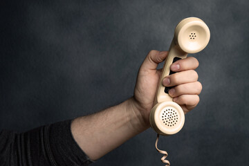 Hand reaching out with landline telephone receiver.