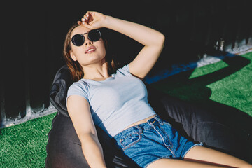 Young hipster girl in sunglasses sitting for little rest after spending time on city with...