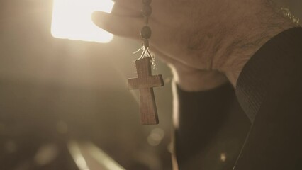 Christian rosary with cross hanging from male hands and swinging close up. Monk holding prayer beads in clasped arms while praying in cathedral closeup. Christianity concept - Powered by Adobe