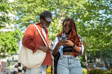 Concerned African American woman focused on smartphone with man stopped on sidewalk to look at map...