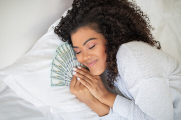 A Hispanic woman is seen laying on a bed with a large amount of money spread out around her. She...