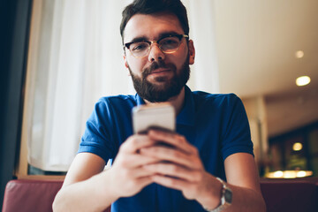 Portrait of young handsome hipster guy in spectacles for vision correction using modern mobile...