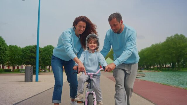 Happy parents educate child ride bicycle with encourage and support. They let go the girl successfully and happily clap