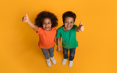 A cheerful African American boy and girl are standing on a bright yellow surface, looking upwards...