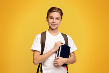 Ready for school. Cheerful boy with backpack holding books, orange studio background
