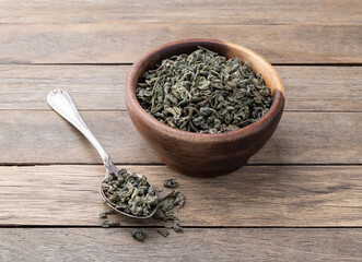 Dried green tea leaves on a bowl over wooden table