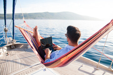 Working in sea traveling. Man with laptop in beach hammock. Summer vacation, living on yacht....