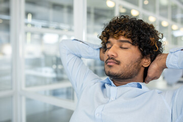 A young man in a light blue button-down shirt relaxes with eyes closed, stretching his neck while...