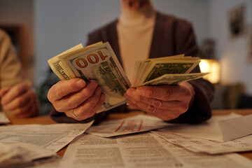 Hands of unrecognizable elderly woman sitting by table with paid and unpaid financial bills and...