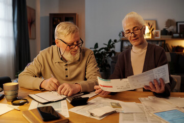Senior couple looking at payment bills in hands of aged woman while checking and discussing financial data in home environment