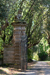 In the summer park there is an ancient stone high gate with an iron lattice, on top there is a statue of a dragon, vertical view