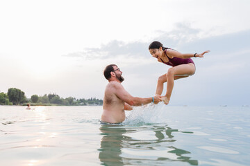 side view at happy girl jumping in the water from the father arms