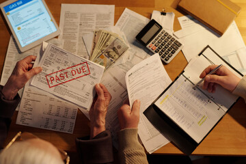 Top view of hands of two senior people sitting by table with financial bills while checking post...