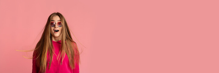Shocked teen girl looking at camera and grimacing, wearing sunglasses, posing isolated on pink...
