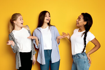 Three multiethnic girls are standing side by side with one of them gesturing animatedly as if in...