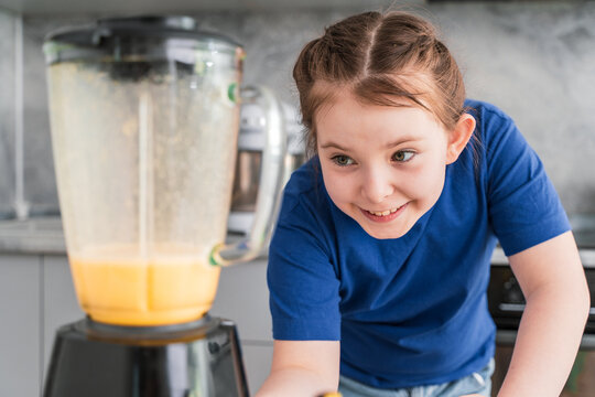 Happy little girl smiling making fruit cocktail in blender, at home in kitchen. Selected Focus
