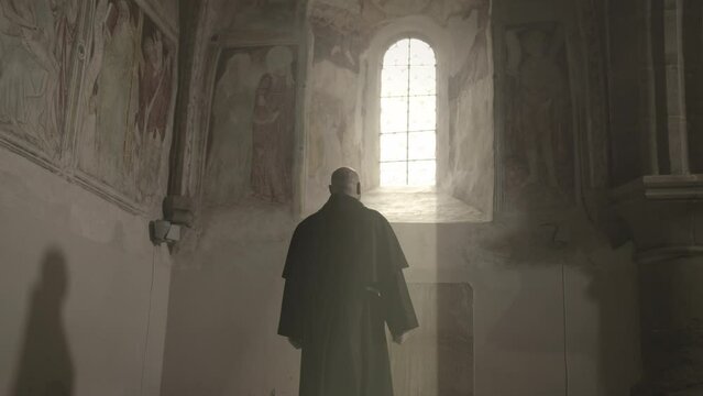 Christian monk wearing robe walking and looking out of window in monastery back view slow motion. Christianity religion, devotion and faith concept