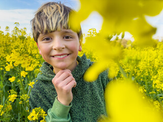 Happy teen smiles among bright yellow canola flowers on field
