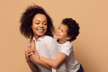 African American woman is holding a child in her arms. The woman is looking down at the child with a gentle expression, beige studio background