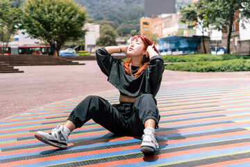 Serene Korean woman with red hair sitting in relaxation on a colorful city square