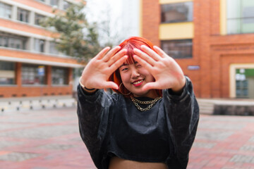 Cheerful Korean woman playfully framing her face with hands in urban setting