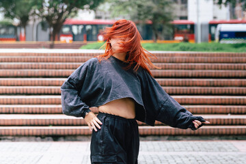 A Korean dancer with fiery red hair performs an energetic twist in an urban park