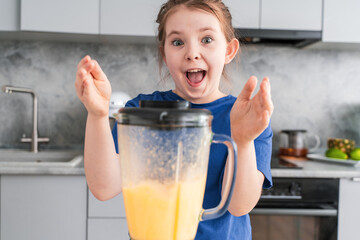 Portrait of a cheerful little girl with a blender in the kitchen. Crazy little girl making fruit...