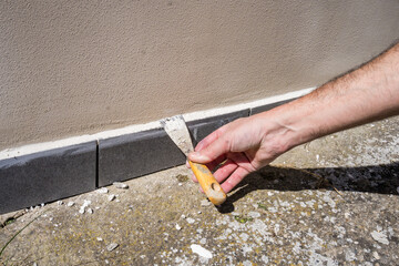 A worker putties the skirting board on the outside of the house, puts the plinth