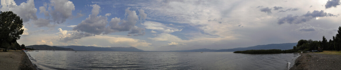 Fototapeta premium Panoramic photo from the shore of Lake Ohrid near Struga. You can see the water, the clouds and the beach.