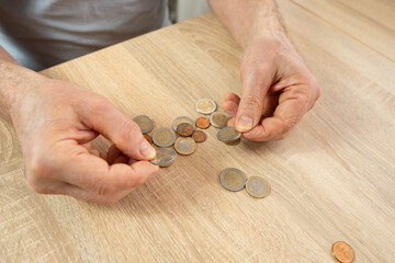 Senior man, poor pensioner lays out euro cent coins on wooden table, counts meager cash money on...