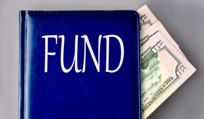 FUND - word on a blue book on a gray background with banknotes