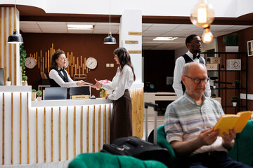 Senior caucasian woman standing at hotel lobby counter and checks in with passport. Female...