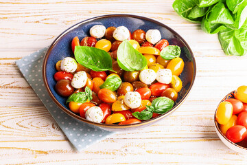 Fresh homemade caprese salad with baby mozzarella cheese, cherry tomatoes, basil leaves and olive oil on rustic wooden table close up. Country style dinner concept.