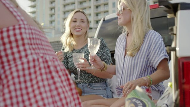 Women eat from a cheese board in the back of a pickup truck at a concert tailgate outdoors