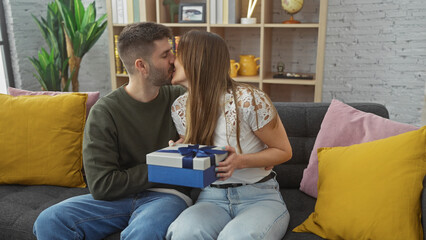 A couple kissing and sharing a gift in a cozy living room, depicting love, affection, and a homely...