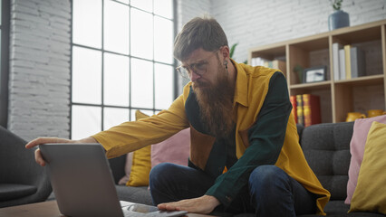Focused bearded man using laptop in modern indoor setting, embodying casual work-from-home...