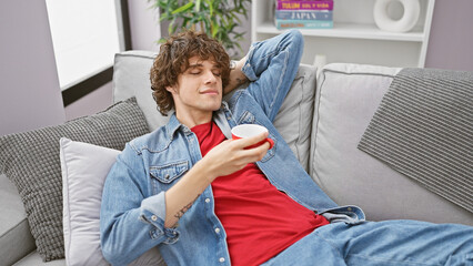 A relaxed young man with curly hair enjoying coffee in a modern living room, exuding casual comfort...