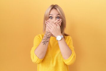 Young caucasian woman wearing yellow sweater shocked covering mouth with hands for mistake. secret...